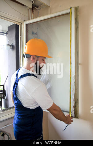 Construction worker and handyman is working on renovation of apartment. Builder is measuring window using measure tape at construction site. Stock Photo