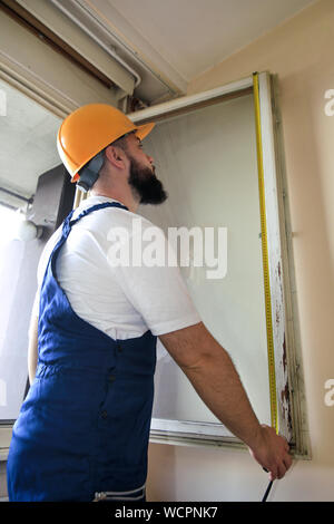 Construction worker and handyman is working on renovation of apartment. Builder is measuring window using measure tape at construction site. Stock Photo