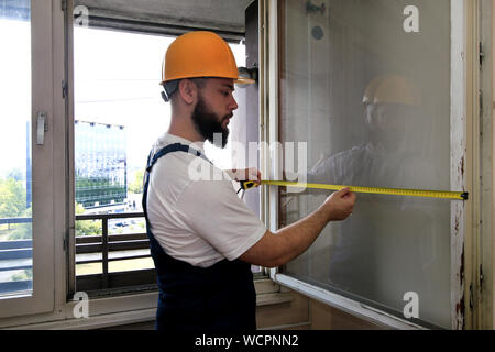 Construction worker and handyman is working on renovation of apartment. Builder is measuring window using measure tape at construction site. Stock Photo