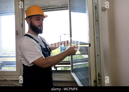 Construction worker and handyman is working on renovation of apartment. Builder is measuring window using measure tape at construction site. Stock Photo