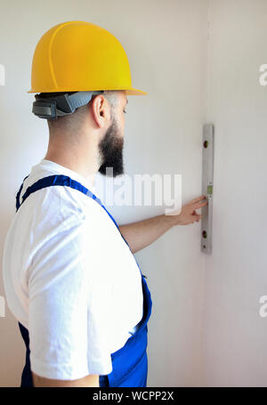 Construction worker and handyman is working on renovation of apartment. Builder is measuring and checking wall room using leveler, spirit level tool. Stock Photo