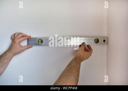 Construction worker and handyman is working on renovation of apartment. Builder is measuring and checking wall room using leveler, spirit level tool. Stock Photo