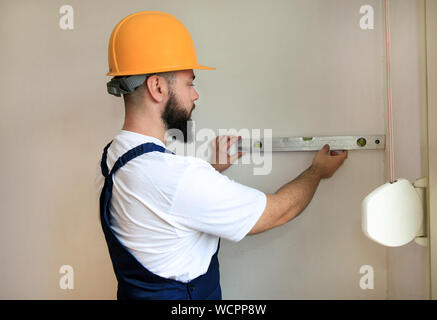 Construction worker and handyman is working on renovation of apartment. Builder is measuring and checking wall room using leveler, spirit level tool. Stock Photo