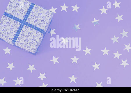 Gift box and star-shaped confetti on a lilac background in neon light. Festive background. Holiday concept. Christmas. Wedding. Birthday. Happy Women' Stock Photo