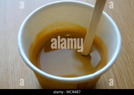 Coffee with foam mixed with a wooden stick, in a disposable paper cup. Ecology, no polyethylene, no plastic. Close-up. Stock Photo
