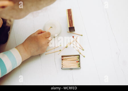 Close up view of child playing with fire, matches and lighting a candle on home room floor. Fire hazard at home concept. Stock Photo