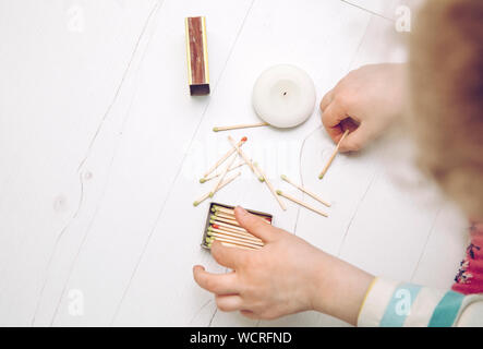 Close up view of child playing with fire, matches and lighting a candle on home room floor. Fire hazard at home concept. Stock Photo