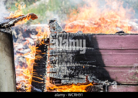 Detail view of burning painted wooden board wall fallen apart, lot of smoke, flames and charcoal. Home house fire concept. Stock Photo