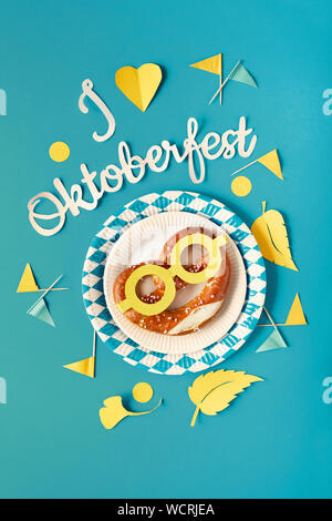 Paper text "I love Oktoberfest", flat lay on paper background with pretzel on paper plate, decorative hearts, flags and Autumn leaves. Stock Photo