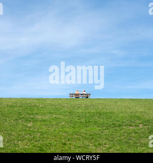 couple sit together on bench placed on top of grassy dike in friesland Stock Photo