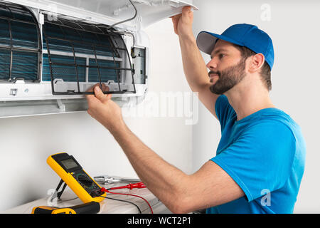 Installation service fix  repair maintenance of an air conditioner indoor unit, by cryogenist technican worker checking the air filter in blue shirt a Stock Photo