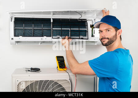 Installation service fix  repair maintenance of an air conditioner indoor unit, by cryogenist technican worker checking the air filter in blue shirt a Stock Photo