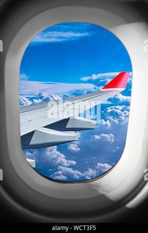 view through airplane window on plane flight wing in front of blue white cloud sky. transportation air travel fly concept Stock Photo