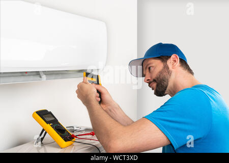 Installation service fix  repair maintenance of an air conditioner indoor unit, by cryogenist technican worker checking the temperature with infrared Stock Photo