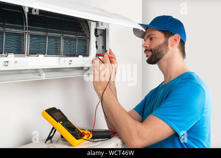 Installation service fix  repair maintenance of an air conditioner indoor unit, by cryogenist technican worker with multimeter checking electric blue Stock Photo