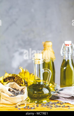 Various types of oil in bottles, dried sunflowers and seeds on wooden table. Close up, copy space. Stock Photo