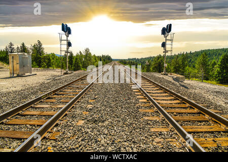 A long set of railroad train tracks disappear as the sun sets in the distance through the mountains in the rural area of North Idaho. Stock Photo