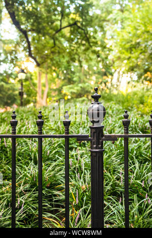 Wrought iron fence against park with green bushes and trees Stock Photo ...