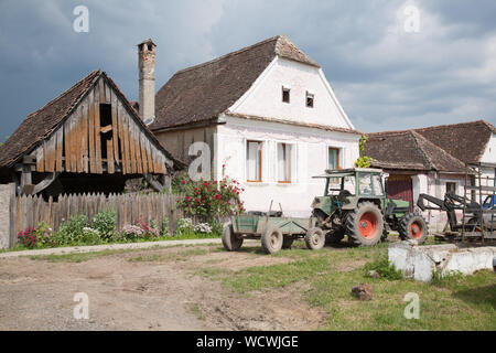 A dilapidated barn, a farmhouse and a tractor with trailer, in the village of Crit, Transylvania, Romania Stock Photo