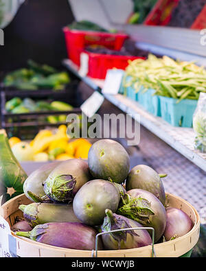 Bushel of egg plant at a roadside stand selling fresh produce.  Additional vegetables in the background, including beans, yellow squash, and cucumbers Stock Photo