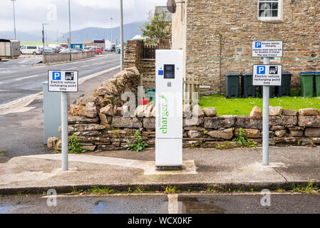 Electric car charging station with a charger and parking signs along a street on a cloudy summer day Stock Photo