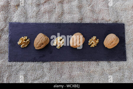 Walnuts, with and without shell, on black table surface, over sack texture Stock Photo