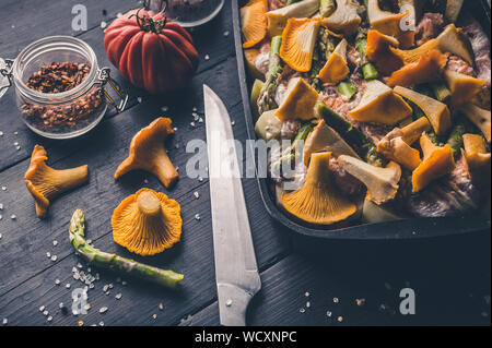 Fresh chanterelles and asparagus in a cast-iron baking dish on a dark wooden table. Stock Photo