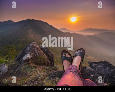 Hiker sitting on mountaintop watching the sunrise over Tea Plantation near Munnar, Idukki District, Kerala, India, Asia Stock Photo