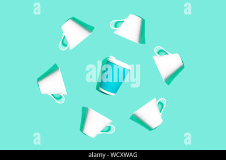 Coffee pattern is made from blue paper cup for coffee and white ceramic cups on bright mint background. Stock Photo