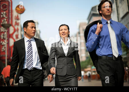Three business colleagues walking down a busy street while talking. Stock Photo