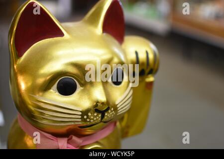 Cute selective closeup shot of a golden cat statue with a pink ribbon Stock Photo