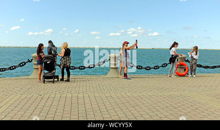 Visitors to Voinovich Park on the Northcoast Harbor in Cleveland, Ohio, USA stand next to Lake Erie during late summer warm weather. Stock Photo