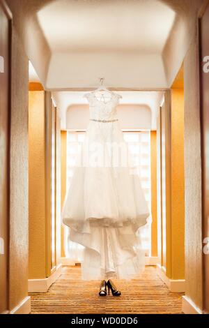 Vertical shot of a beautiful wedding gown on a stand with a pair of black high heels below Stock Photo