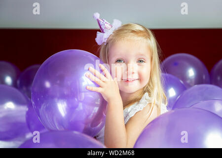 Cute little girl in stylish dress celebrating birthday day with purple balloons Stock Photo