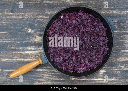 Fried blue cabbage with onion, apple and garlic in frying pan on wooden table. Top view, close up Stock Photo