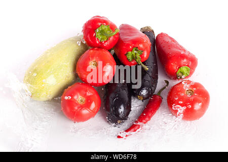 Tomatoes red sweet peppers hot chilli peppers, violet eggplants, green zucchini in jet of water drops of water on white background closeup isolated Stock Photo