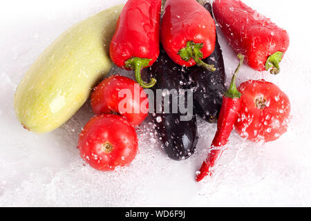 Tomatoes, red sweet peppers, hot chilli peppers, eggplants, green zucchini, jets of cool drops of water on white background closeup top view isolated Stock Photo