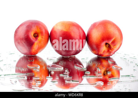 Three peaches on a white mirror surface in drops of water isolated macro Stock Photo