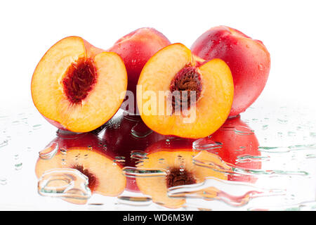 Whole peaches and two halves of a peach with a stone inside on a white mirror background with reflection in water drops close up isolated Stock Photo