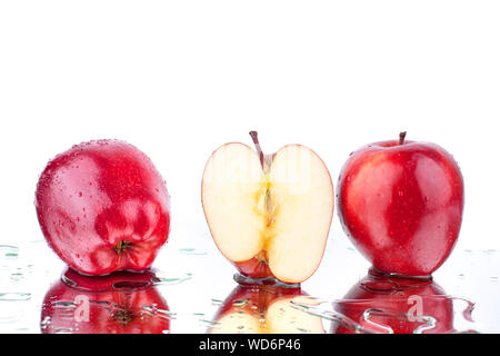 Red apples whole and half in drops of water on white mirror background with reflection isolated close up Stock Photo