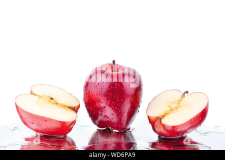 One whole red apple and two halves of apple in water drops on mirror white background with reflection isolated close up Stock Photo