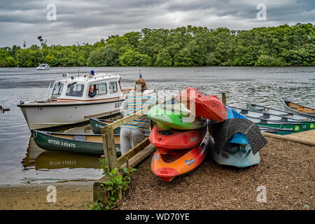 Man standing beside colorful hire canoes talking to a Norfolk Broads Ranger, who is sat in his boat, on Salhouse Broad in Norfolk Stock Photo