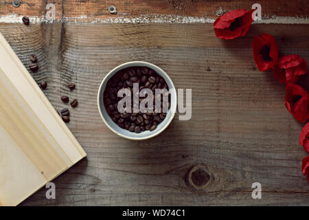 Coffee beans, old book and red flowers on wooden background Stock Photo