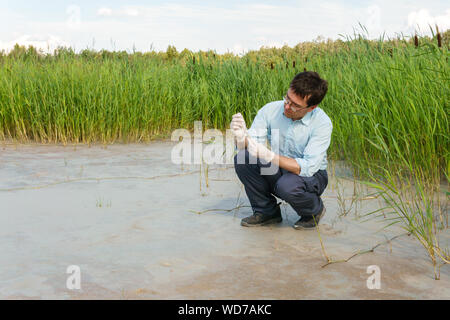 field researcher biologist examines a sample of soil in a test tube against a dry marsh Stock Photo