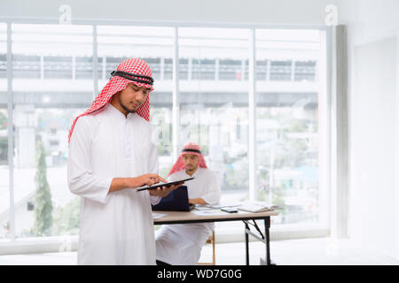 Arabian Businessman Using Tablet for Communication Business Dealing in Office Workplace, Arab Man Entrepreneurs in Traditional Clothes is Working Comm Stock Photo