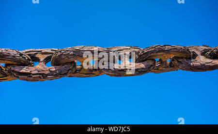 A very old and rusty thick iron chain isolated against a blue sky. Stock Photo