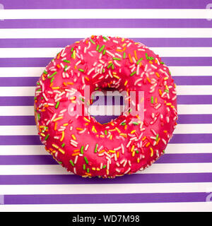 Pink donut in multicolored sprinkles on  background strips of white and purple top view in a square Stock Photo