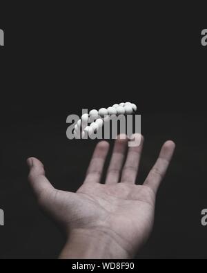 Shallow focus shot of a male's hand throwing white beads upwards on a dark background Stock Photo