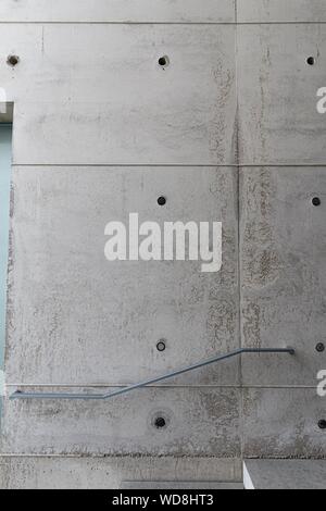 Vertical shot of a gray wall with holes and a metal handrail Stock Photo