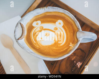 Close-up teddy bear latte art coffee in handmade ceramic cup on wooden tray on white background, top view. Stock Photo